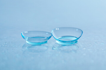 Pair of contact lenses and water drops on light mirror surface, closeup