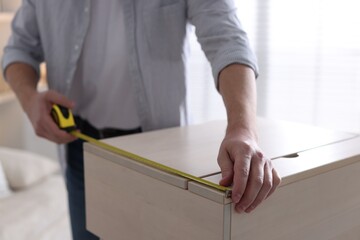 Man measuring wooden cabinet with tape indoors, closeup