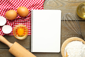 Blank recipe book, eggs, flour and kitchenware on wooden table, flat lay