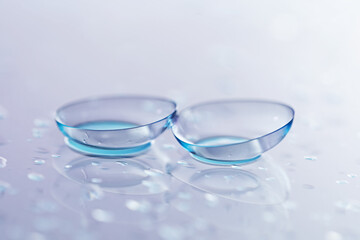 Pair of contact lenses and water drops on light mirror surface, closeup