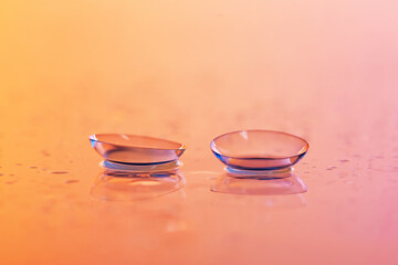 Pair of contact lenses and water drops on color gradient mirror surface, closeup