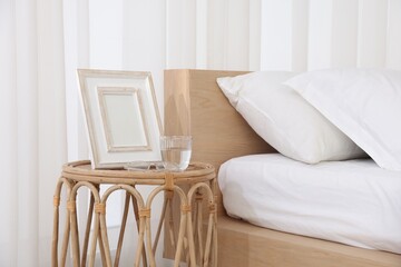 Bedside table with picture frame and glass of water near bed in room
