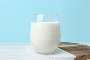 Glass of fresh milk on white wooden table against light blue background