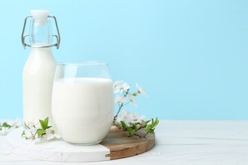 Fresh milk and blossoms on white table against light blue background. Space for text