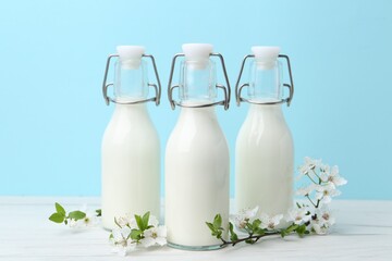 Fresh milk and blossoms on white table against light blue background