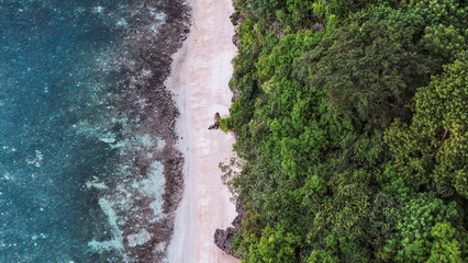 Top down coastal view of bright aqua water meeting dramatic tropical cliffs and shoreline.