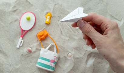 A hand holding a paper airplane on a beach with a tennis racket, a camera
