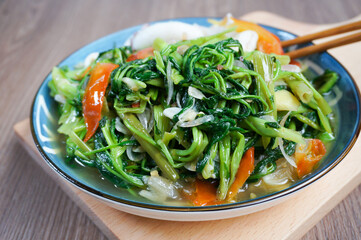 Stir-fried water spinach, on a blue plate, on a chopping board, with a wooden background,