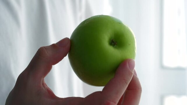 Green apple in hands of man in white t-shirt.
Man holds ripe apple in hands.
Close-up of ripe and green apple