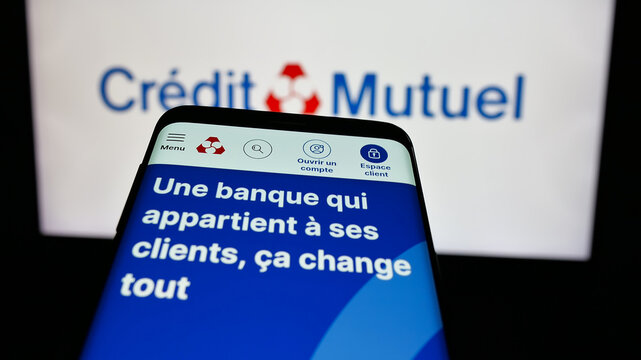 Stuttgart, Germany - 03-21-2025: Mobile phone with logo of French bank Caisse Federale de Credit Mutuel on screen in front of website. Focus on top-left of phone display.