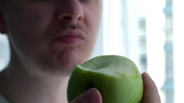 A juicy and ripe apple in the hands of a man.
A man chews a green apple with his mouth.
A man bites a tasty apple