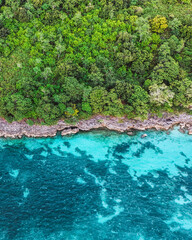 Bright turquoise sea meets lush green island cliffs and tropical forest. Summer vacation and summer holiday concept