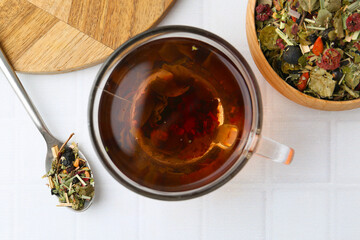 Delicious herbal tea and dry leaves on white tiled table, flat lay