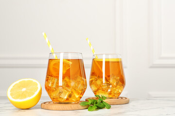 Refreshing iced tea with slices of lemon, mint and drinking straws on white marble table