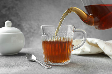 Pouring freshly brewed tea from teapot into cup at grey table, closeup