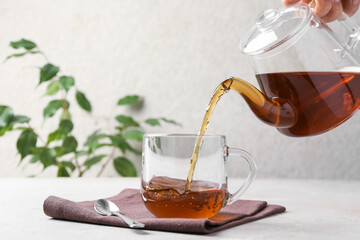 Woman pouring aromatic tea from teapot into cup at light textured table, closeup