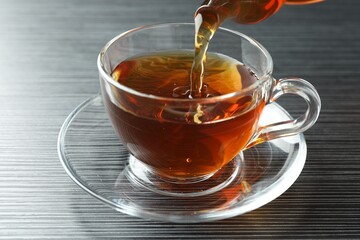 Pouring aromatic tea into cup at black wooden table, closeup