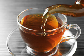Pouring aromatic tea into cup at black wooden table, closeup