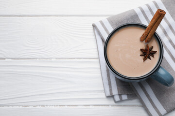 Aromatic Masala tea in cup, cinnamon and anise star on white wooden table, top view. Space for text