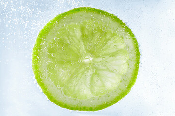 Soda water with lime slice against white background, closeup