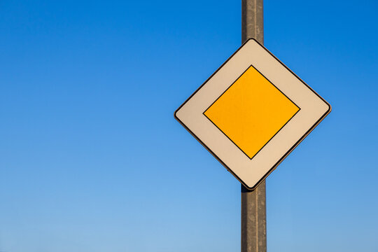 priority road traffic sign with yellow diamond shape on pole against clear blue sky symbolizing main road and traffic regulations on sunny day outdoors
