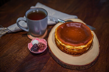 Basque cheesecake with a cup of tea and a few chocolates on a dark wooden table