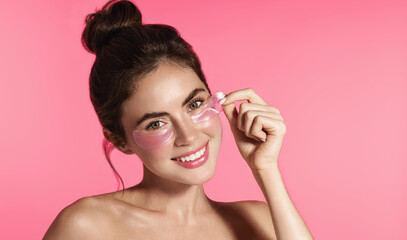 Close up portrait of beautiful, smiling young female model, applies hyaluronic under-eye patches from puffiness and dark circles, using skincare treatment, cosmetology and beauty concept