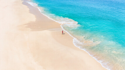 Ocean waves lap at the shore of a tropical beach with white sand from aerial view