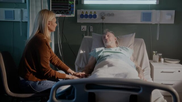 Daughter sits near elderly father lying on bed in clinic ward