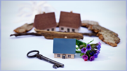Ein kleines freistehendes Häuschen, ein Schlüssel, Blumen. Konzept Hauskauf.