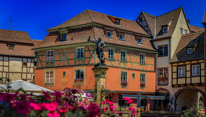 Fototapeta premium Ornate half timbered houses with blooming flowers near the Schwendi Fountain, Little Venice district in Colmar, picturesque village in Alsace, France