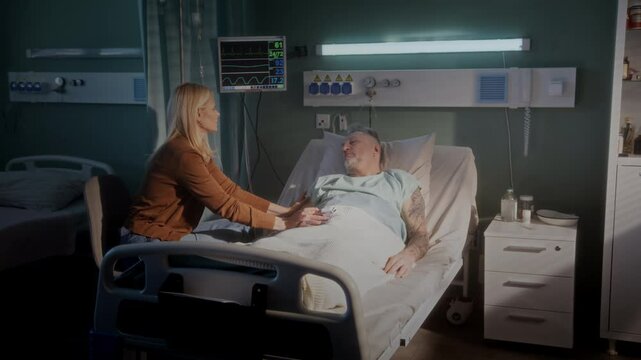 Old man lies under blanket looking weak daughter sits in ward