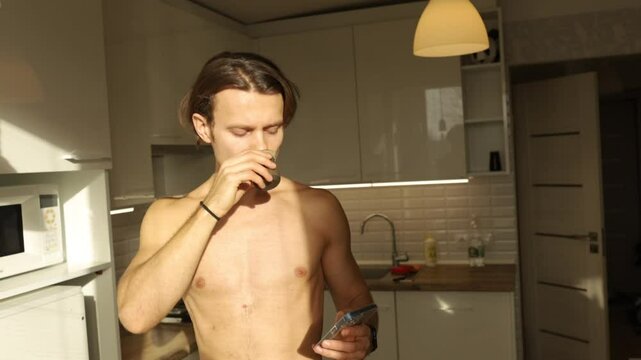 a man with a naked torso drinks puer tea in the kitchen in the morning