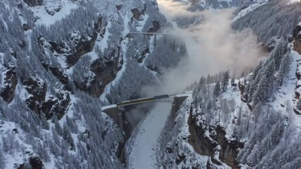 Yellow train crossing snowy mountain bridge in winter