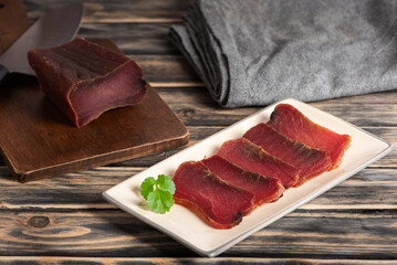 Slices of mojama on a plate and next to a cutting board with a piece, salt-cured tuna loin, rustic background.