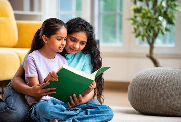 Happy Indian Asian mom and daughter bonding while reading a book on the floor at home