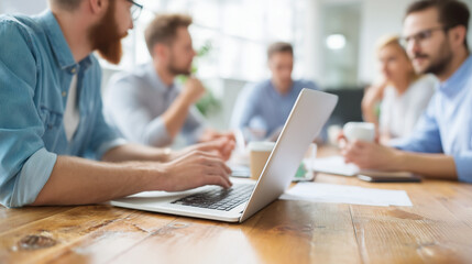 Obraz premium Team of professionals collaborating at a table with a laptop during a meeting in a bright, modern office setting.