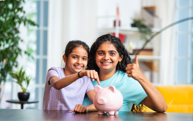 Mother and daughter save money at home, placing coins in piggy bank to build good financial habits