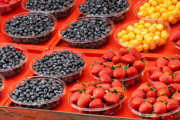 Fresh seasonal berries - strawberries, blueberries, and physalis in containers on a bright market stall.