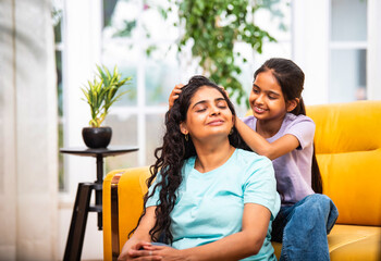Indian mom enjoys a gentle oil head massage from her daughter while relaxing on the sofa