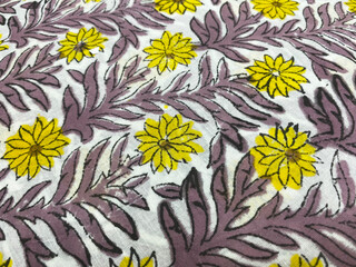 Close-up of hand block printed yellow blooms intertwined with purple creepers on pristine white...