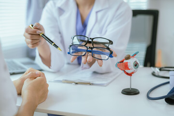 A female doctor talks to an elderly patient who is being shown a modern eye model in a hospital.