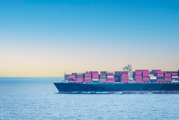 Large, fully loaded, cargo container ship sailing through calm, blue Indian Ocean. International trade route.