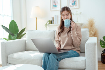 Young Woman Enjoys Working on a Laptop While Sipping Coffee in a Cozy Living Room Setting