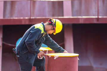 A crew member on the deck of a container ship preparing to paint hazard markings in a striped...