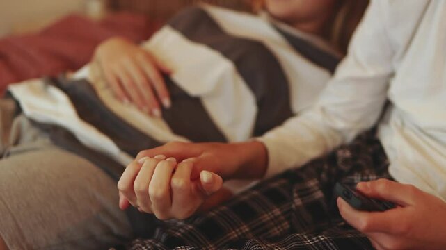 Caring siblings embracing on bed, sharing intimate connection, holding hands closely with smartphone resting nearby