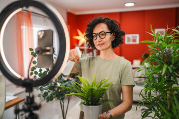 Mature woman have live stream on mobile phone about home plant care