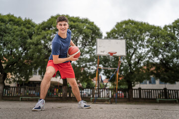 Fototapeta premium One caucasian teenager stand on basketball court with ball