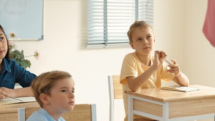 Caucasian smart student listening teacher explaining about classwork. Young teacher standing at blackboard and talking about lesson while children learning or studying at school. Education. Pedagogy.