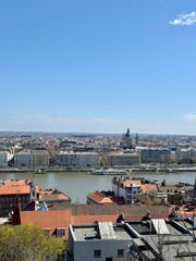 Fototapeta premium Panoramic view of Budapest with the Basilica, Danube River, and red-roofed buildings under a clear blue sky, captured from the Buda side on a sunny spring day.